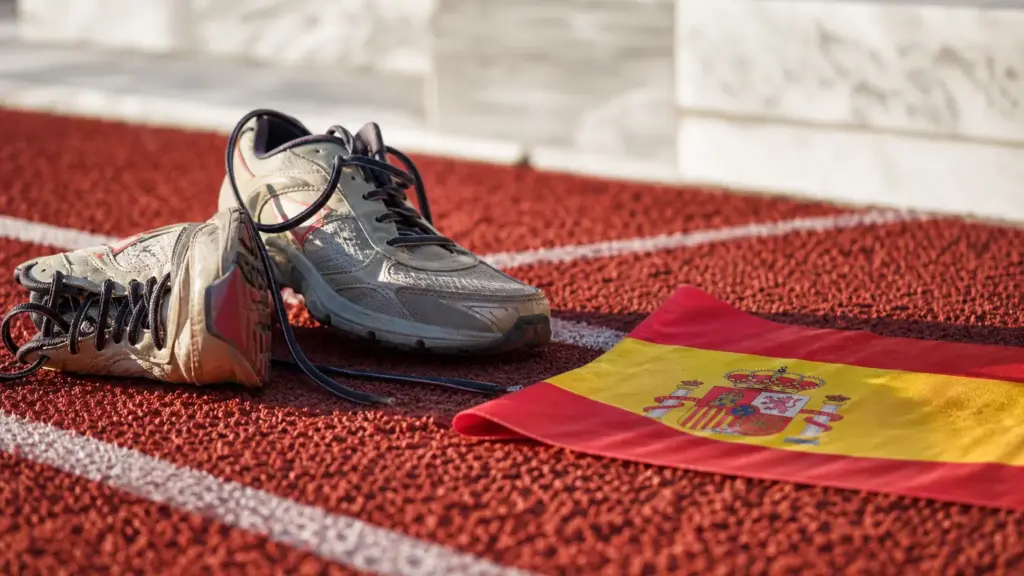 maratón de atenas: detalle de pista roja con líneas blancas, zapatillas y una bandera de España al atardecer