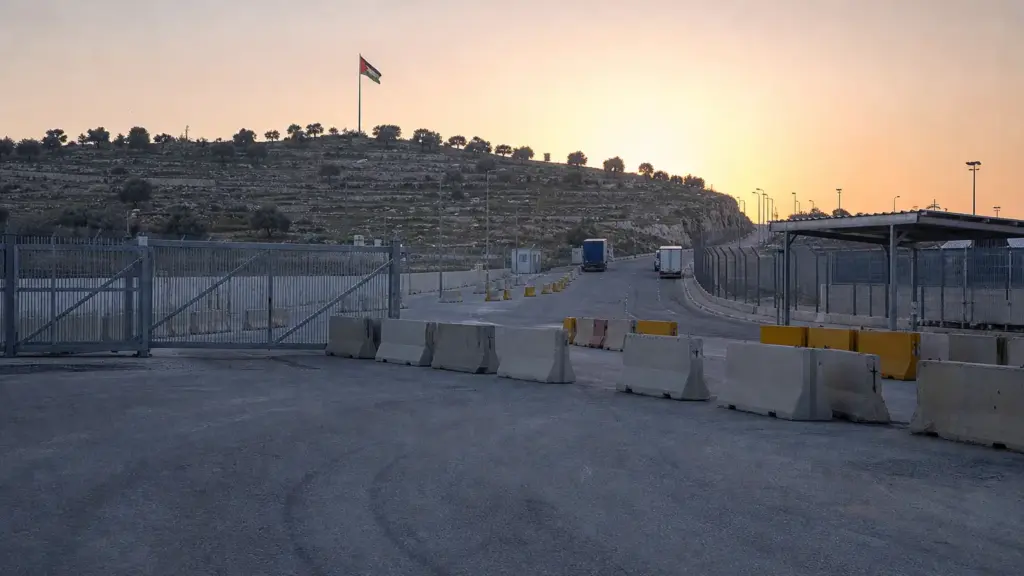 economía palestina: paso comercial vacío con portones cerrados y barreras de hormigón entre colinas de olivos al amanecer