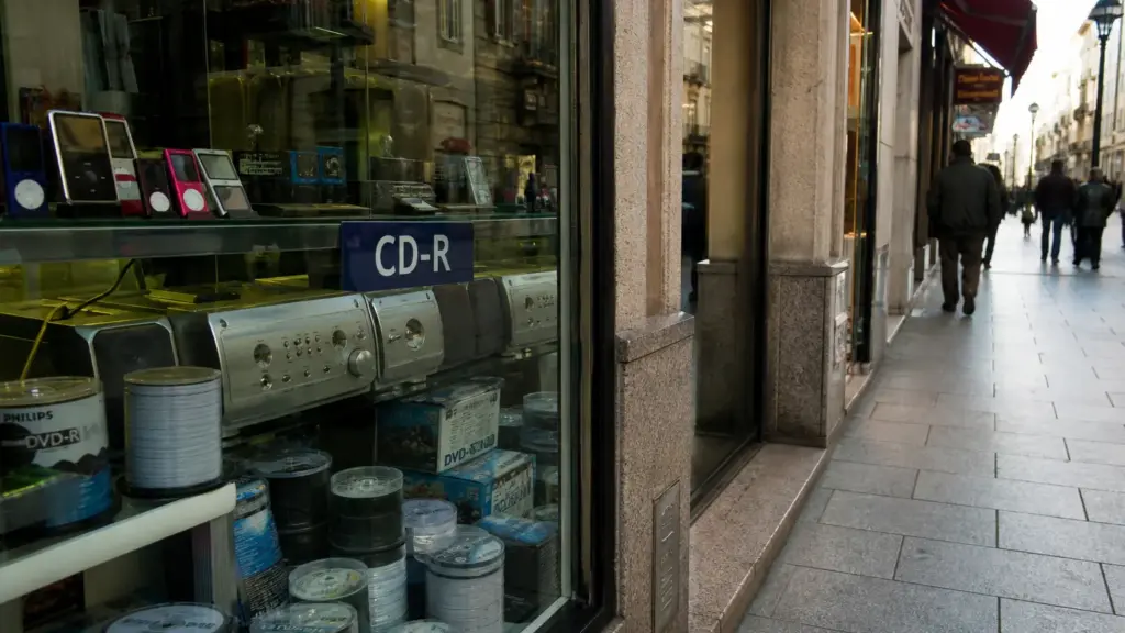 facua contra el canon: escaparate de una tienda con CD y DVD vírgenes y reproductores en una calle comercial con peatones de espaldas