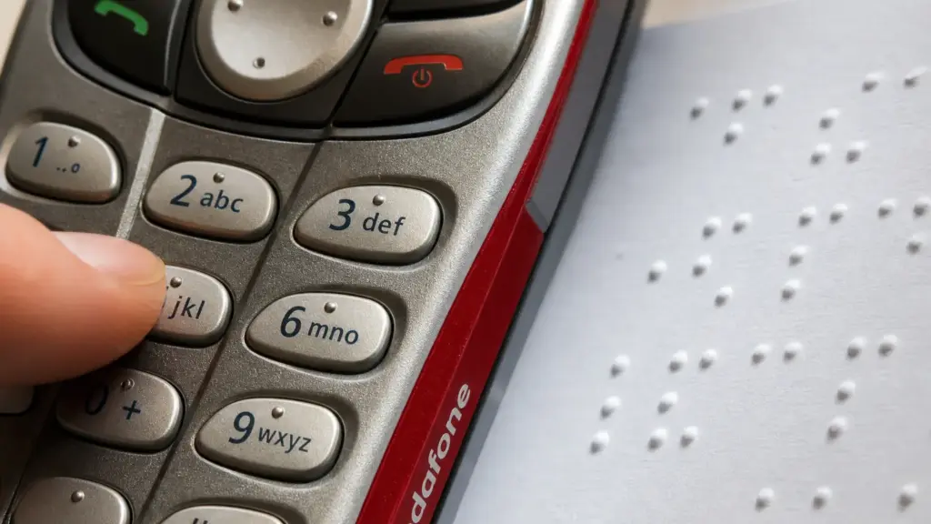 vodafone speaking phone: teclado de un móvil junto a una hoja con puntos en braille iluminada por luz natural