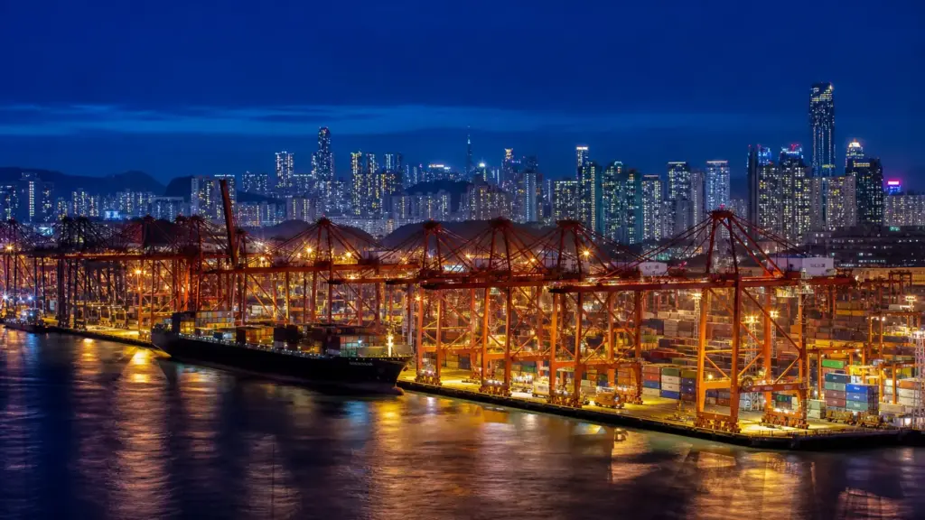 crecimiento de asia oriental: puerto de contenedores iluminado de noche con grúas y el perfil de una ciudad al fondo