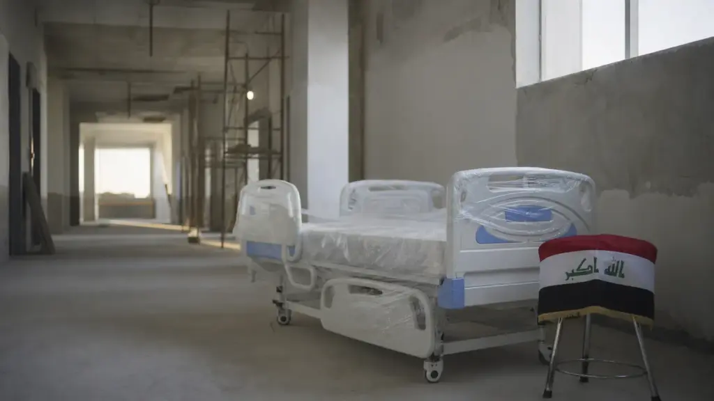 sanidad de irak: cama de hospital nueva envuelta en plástico junto a una bandera iraquí en un pasillo en obras