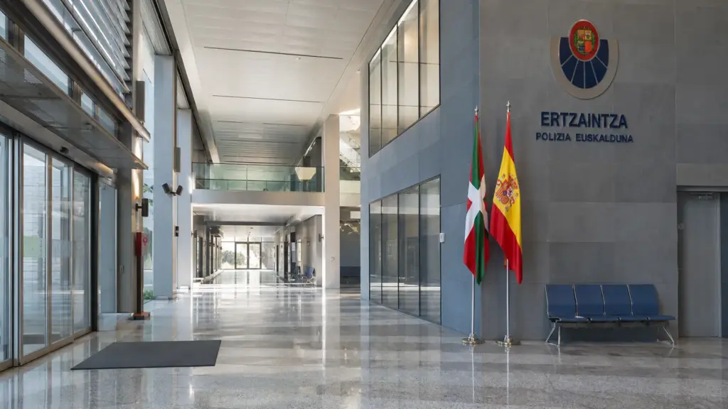 cuotas en la ertzaintza: vestíbulo vacío de una comisaría con la ikurriña y la bandera de España a la luz de la mañana