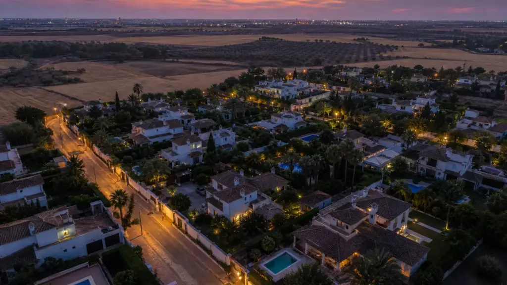 alba silva: vista aérea al atardecer de una urbanización de chalés con piscinas rodeada de olivares a las afueras de Sevilla