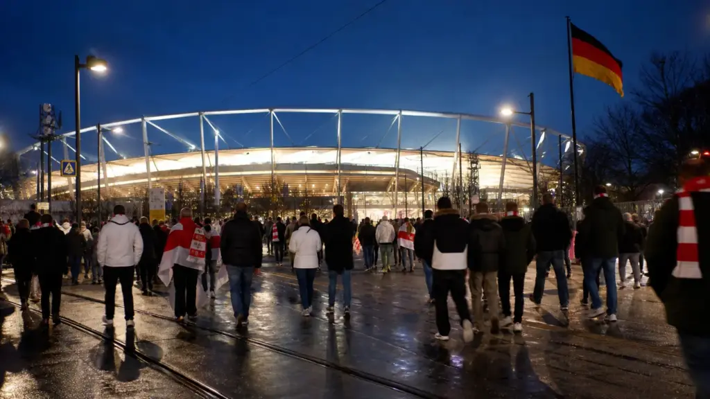 atlético en stuttgart: aficionados de espaldas caminan de noche hacia un estadio iluminado con bufandas rojiblancas