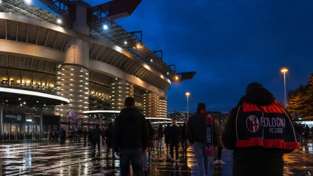 bologna ante el milan: aficionados de espaldas caminando hacia el estadio de San Siro iluminado al anochecer