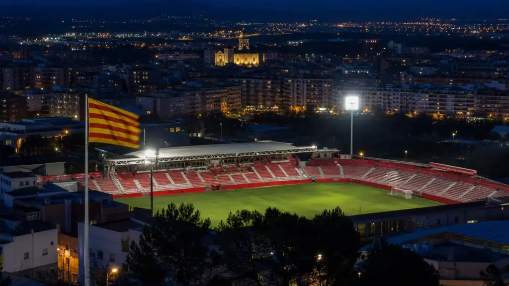 girona y andorra: estadio de fútbol iluminado de noche en Girona con luces de la ciudad al fondo