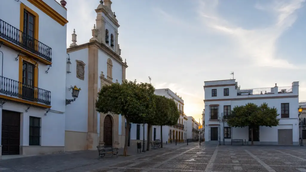 eduardo martín clemens: plaza encalada del barrio de Santa Cruz de Sevilla con una iglesia y naranjos al amanecer