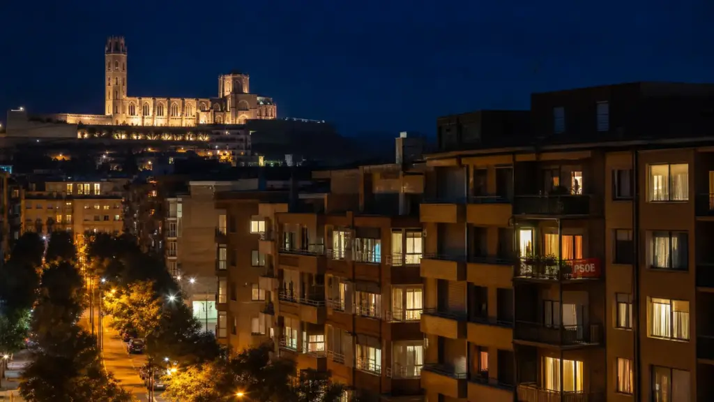 rebeca torró: edificios de viviendas con ventanas iluminadas de noche en Lleida, con la Seu Vella al fondo