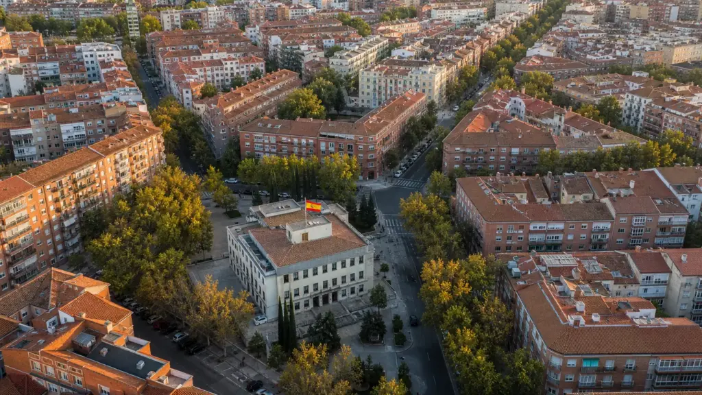 subsidio de 52 años: vista aérea de un barrio residencial con tejados rojizos y una bandera de España en un edificio público
