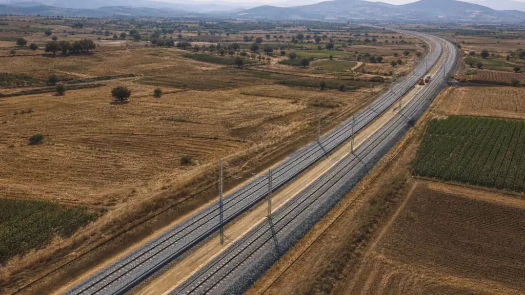 tren incendiado en ricla: vista aérea de una vía de alta velocidad entre campos de cultivo con equipos de mantenimiento a lo lejos