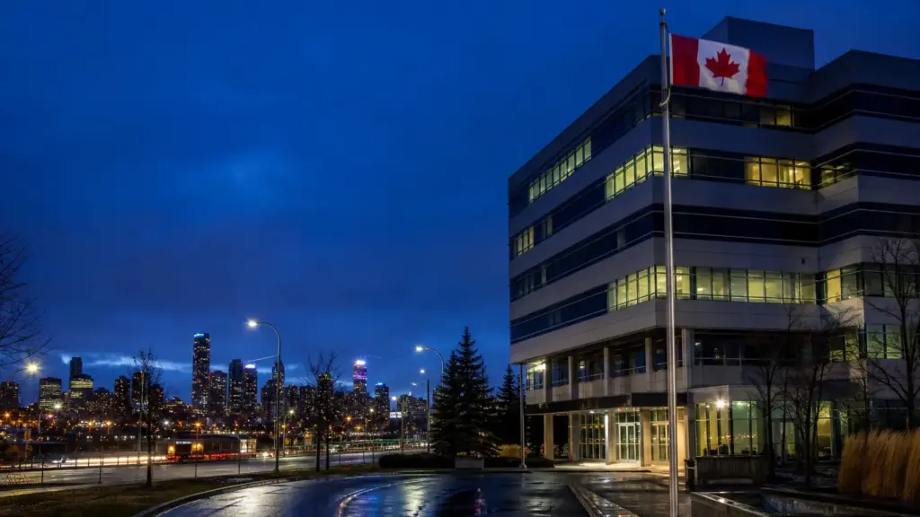 cierre de bioware: edificio de oficinas con pocas ventanas iluminadas de noche en Edmonton junto a una bandera de Canadá
