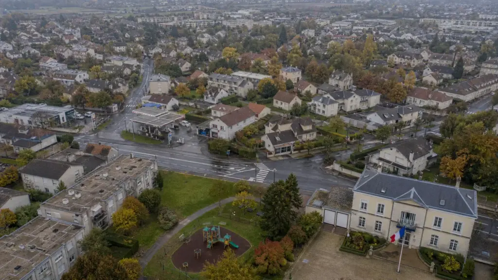 tiroteo en trappes: vista aérea de un barrio residencial con una carretera, un parque y una bandera de Francia bajo un cielo nublado
