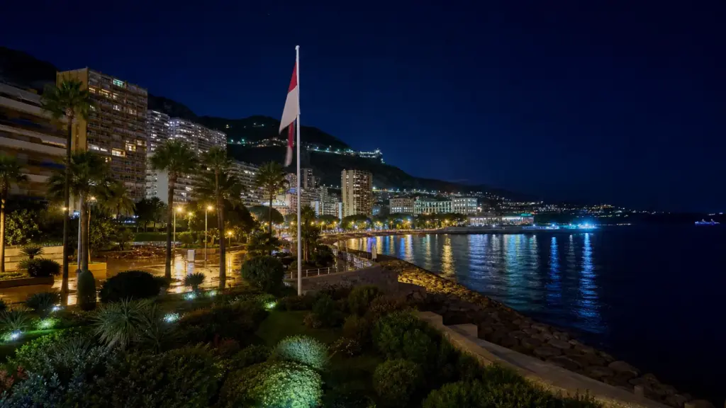 antoine de massy: jardín junto al bulevar del Larvotto en Mónaco de noche, con farolas encendidas y la bandera monegasca