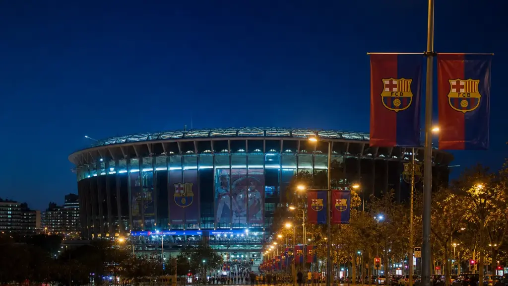lamine yamal y mbappé: estadio iluminado de noche en Barcelona con banderas azulgranas en las calles