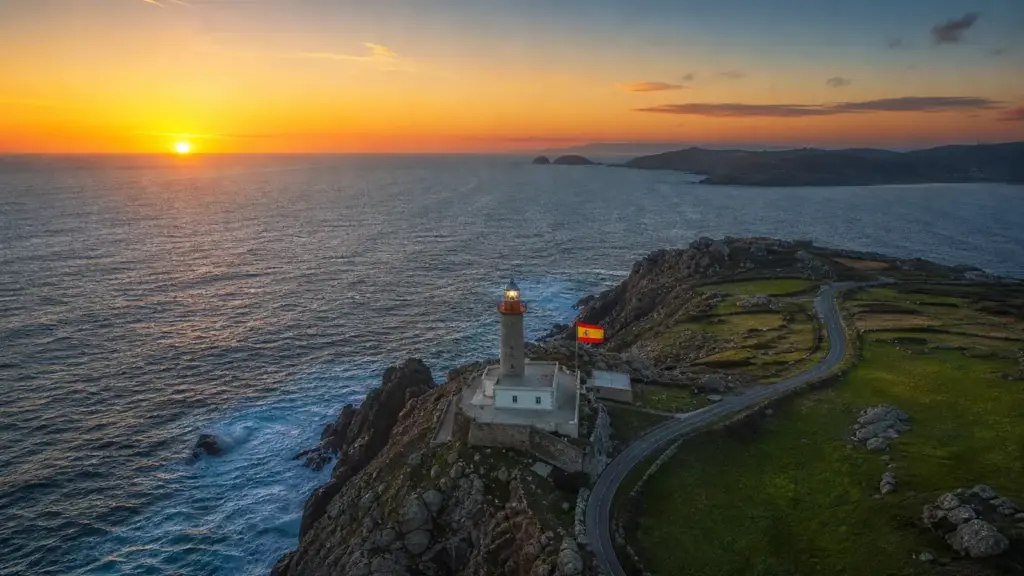 cambio horario en españa: vista aérea de un cabo de la costa gallega con un faro al atardecer