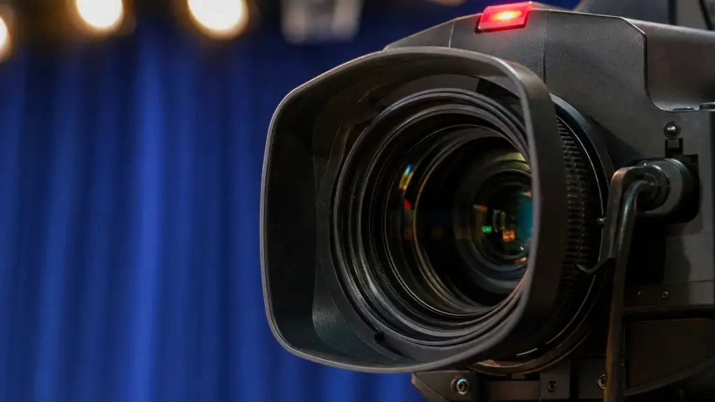 regreso de maría patiño: detalle de la lente de una cámara de televisión con luces de plató al fondo