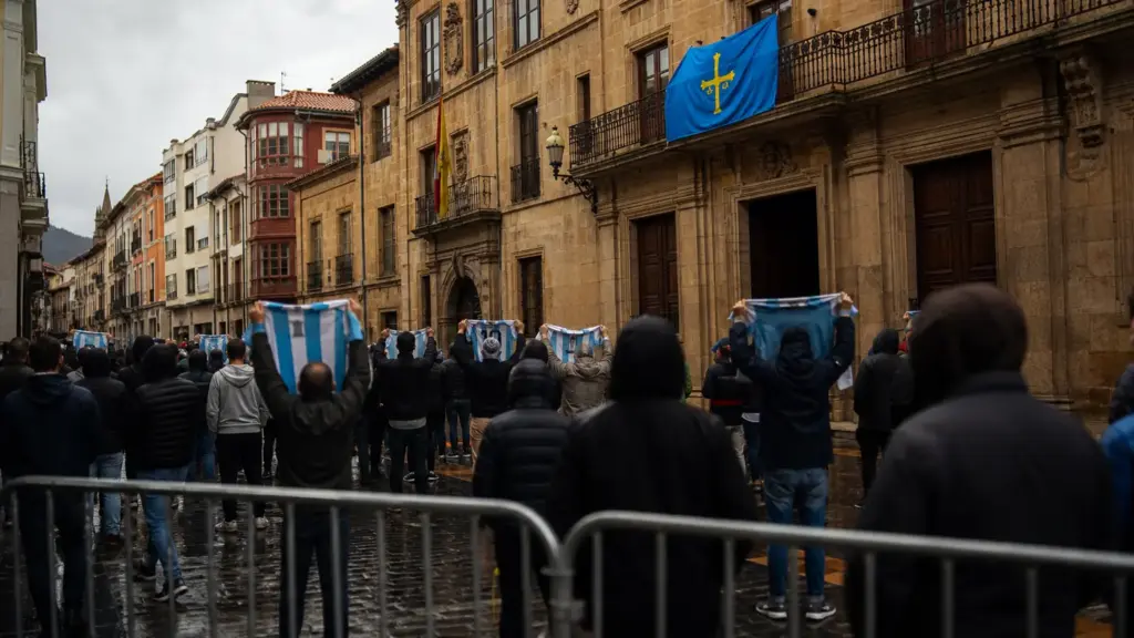 messi en oviedo: aficionados de espaldas con camisetas albicelestes frente a un edificio de piedra con la bandera de Asturias