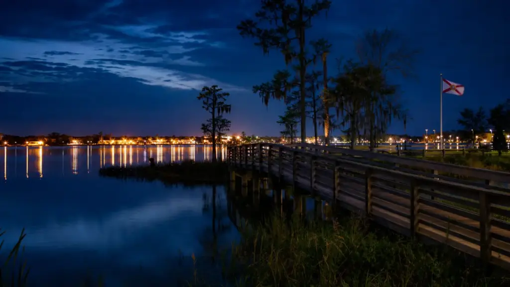 caimán en winter garden: orilla de un lago con un puente de madera de noche y luces de la ciudad a lo lejos