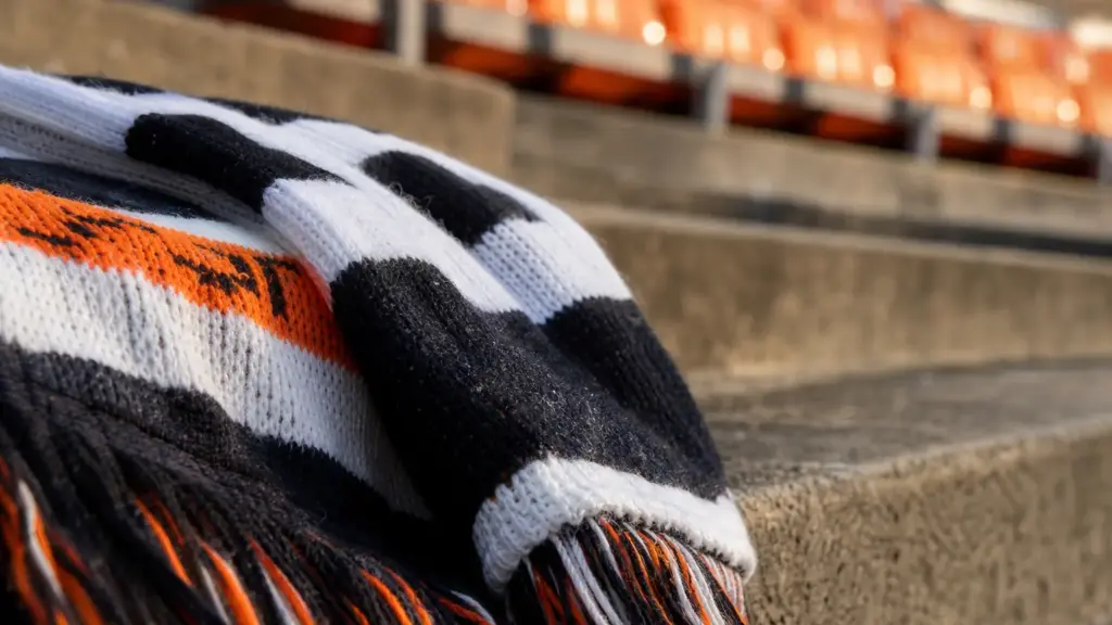 pitchwise holdings: bufanda de lana blanca, negra y naranja sobre las gradas de cemento de un estadio al atardecer
