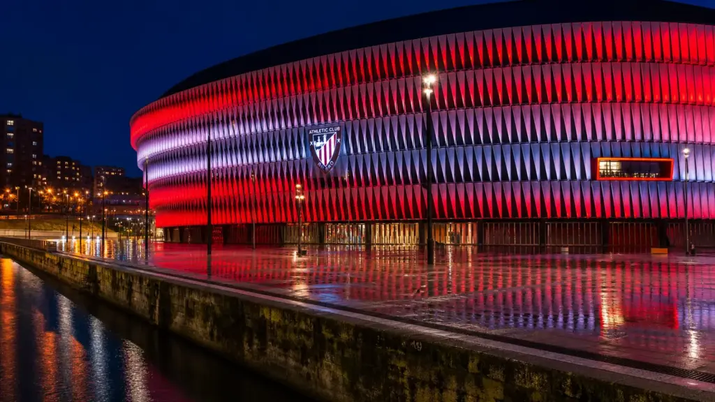 athletic ante el getafe: estadio iluminado de rojo y blanco de noche en Bilbao junto a la ría
